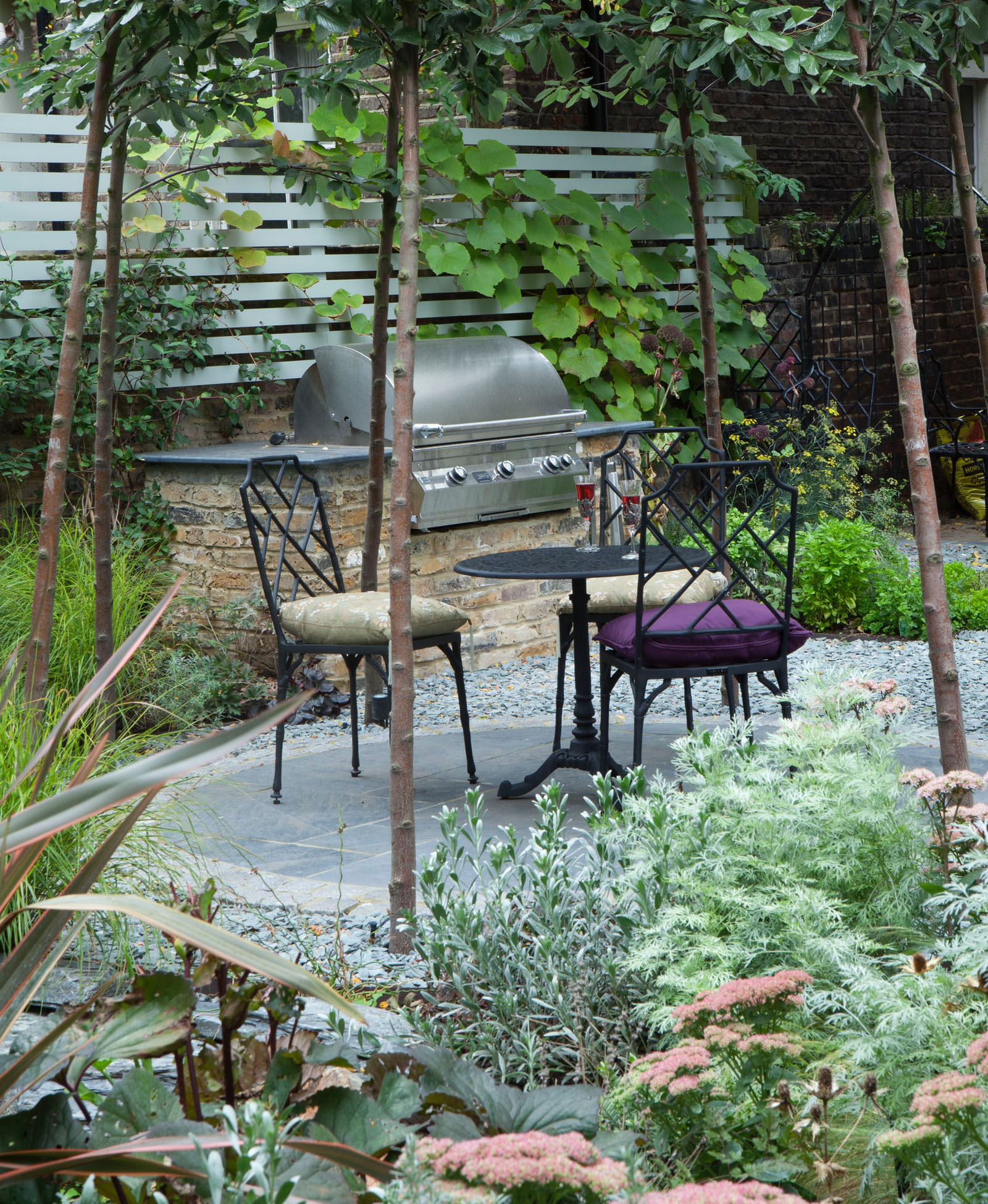 The herbaceous planting at the front overlooks the slate paving seating area. Some Sorbus are tied together to form an arch above the table and chairs in this Belsize Park garden, London.
