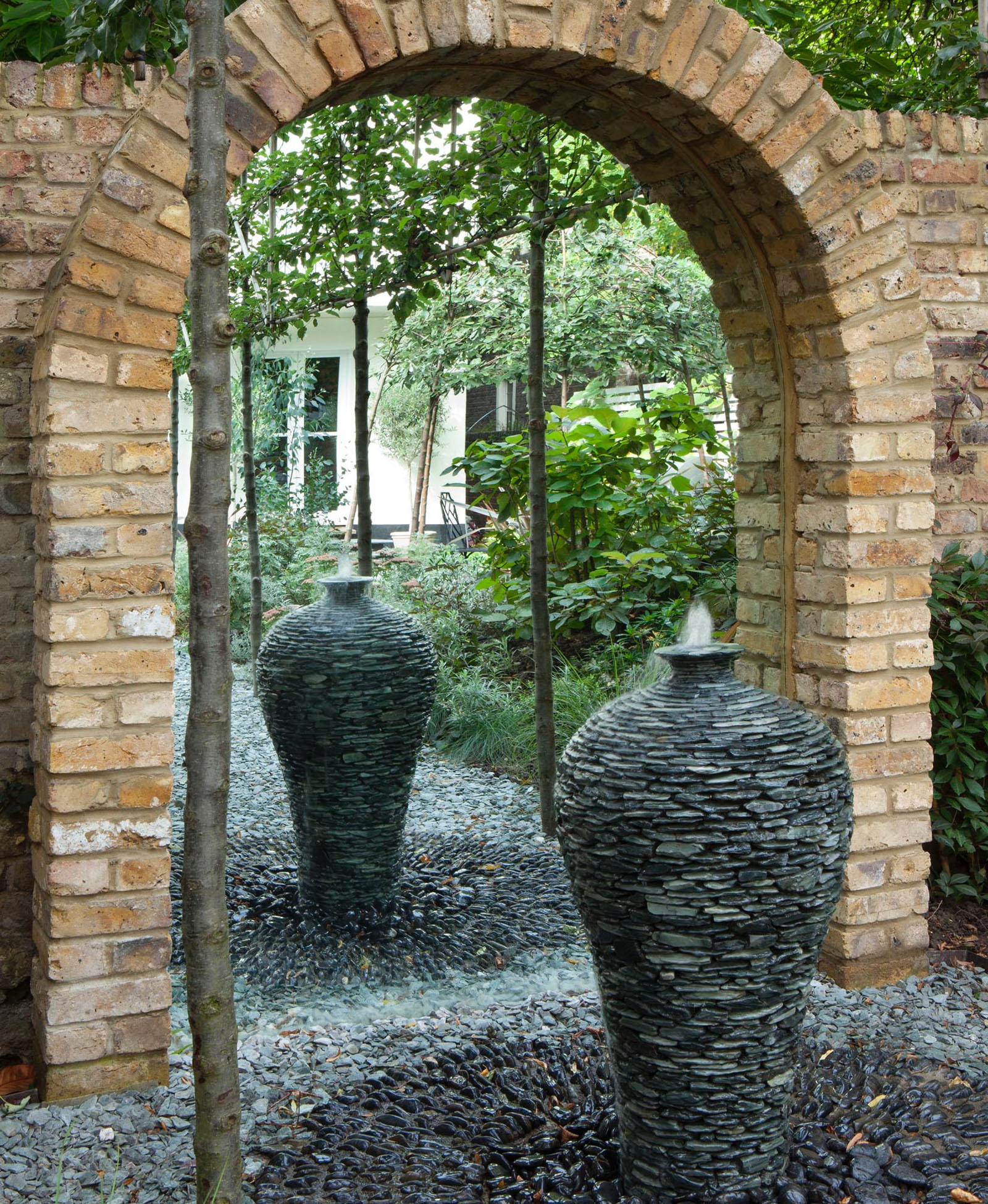 A brick arch has been built by the landscapers to fit in a mirror to reflect the whole Belsize Park garden, starting with a bespoke water feature installed on black slate chips and gravel.
