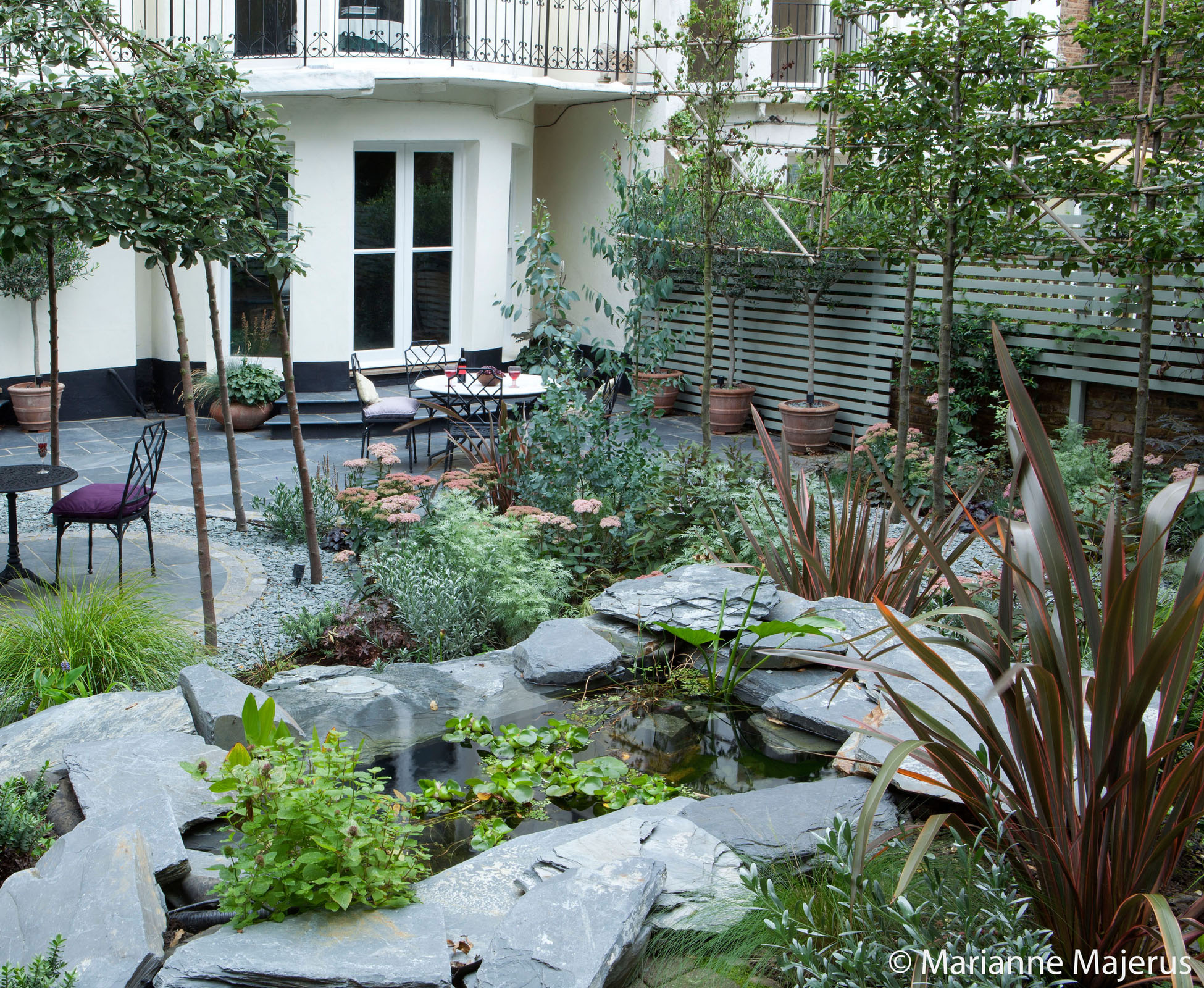 The water feature has been built on a slope using slate pieces. It is visible from everywhere in this Belsize Park garden and from the house. The eclectic planting around it helps to make it disappear beneath the foliage.