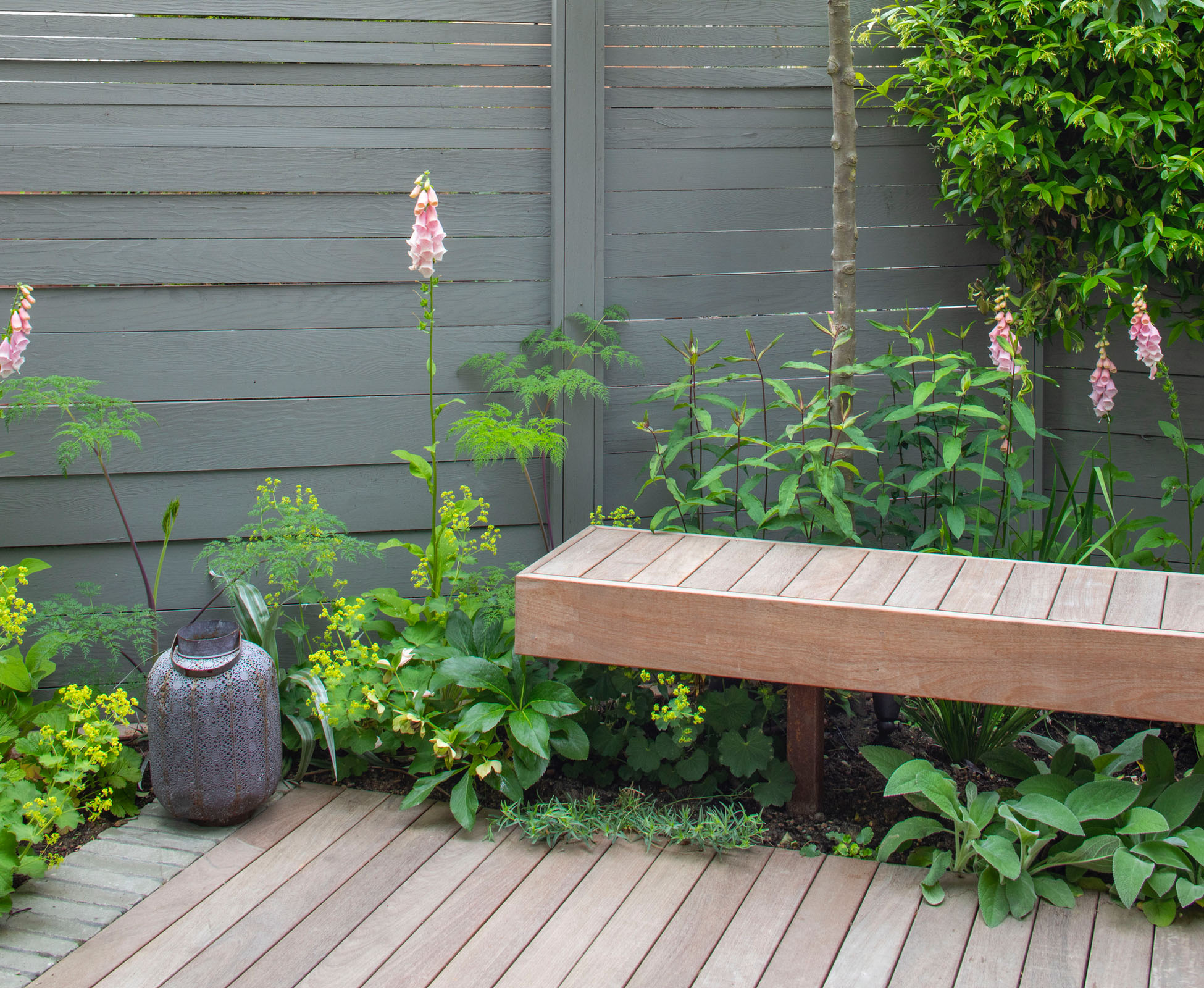 A floating hardwood timber bench sits at the edge of the deck with lush planting spilling out from underneath the Bounds Green Garden boundary.