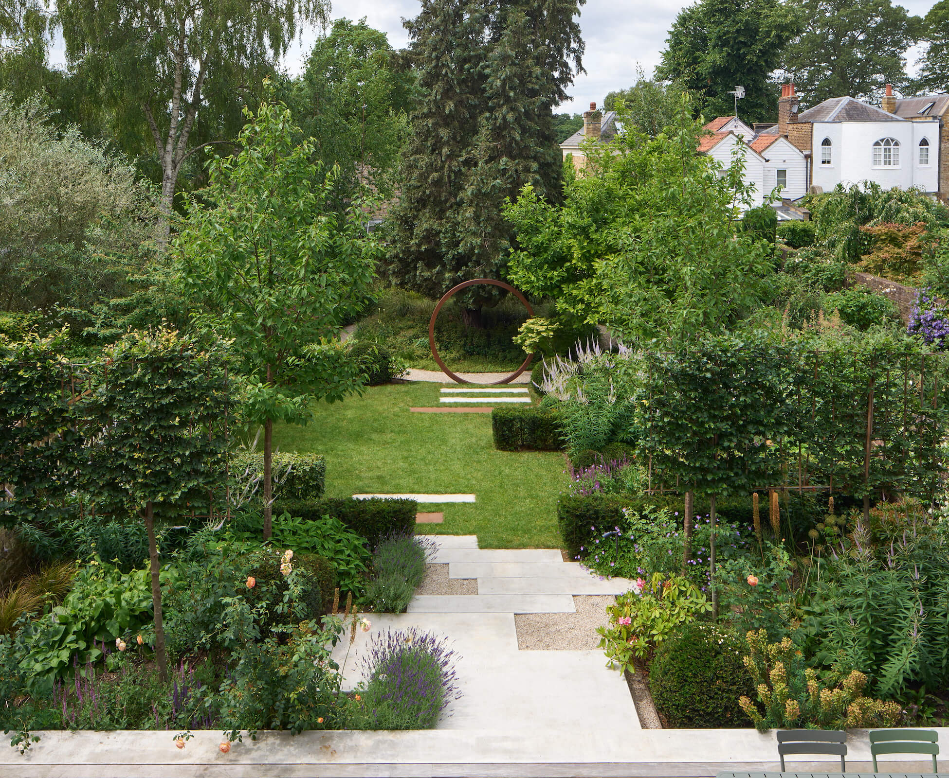 A birds eye view of the garden from the first floor, showing the staggered linear design of the poured concrete stepping stones, balanced by the stepped hedging and planting.