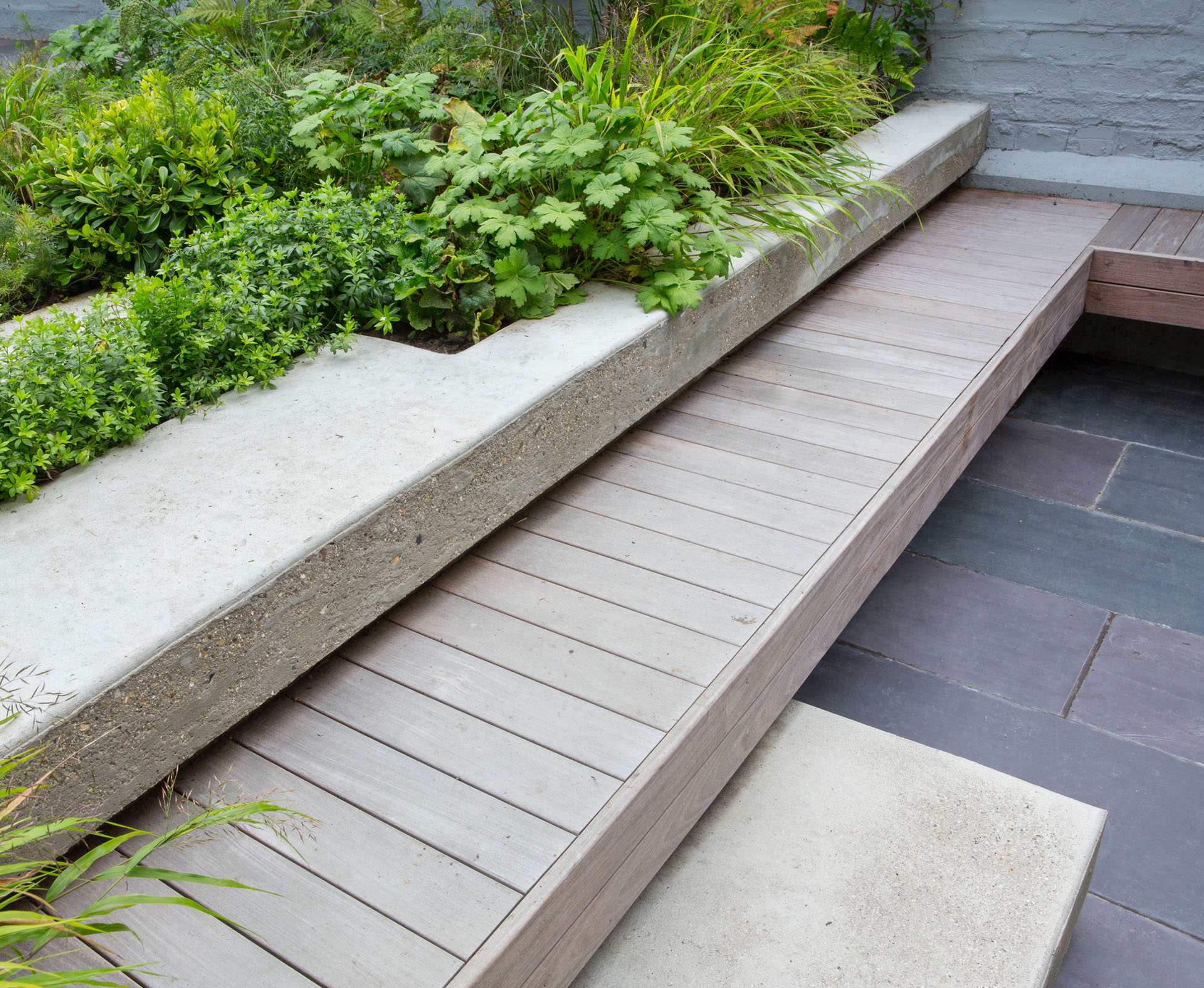 The shadow gap under the poured concrete step is visible on the built in hardwood ipe bench, floating above the reclaimed slate paving in this Crouch End garden.