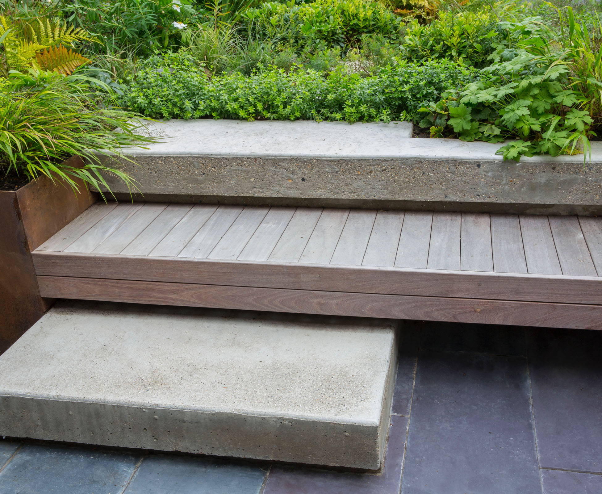 The bespoke built in ipe timber bench wraps around the lower patio area, wide and comfortable, and becomes a step to access this Crouch End garden. It floats above the slate paving and poured concrete, fixed to the Corten steel retaining wall.