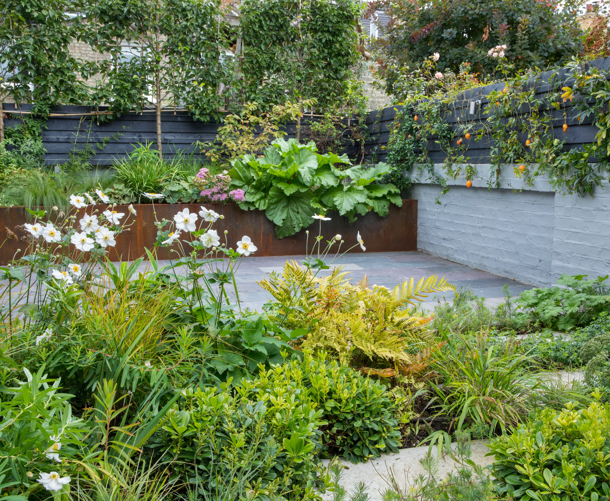 The green and white planting scheme looks wild in this Crouch End garden, in North London whilst the hard landscaping is simple, following a strong geometric design. The colours of the rusted Corten steel, the reclaimed slate paving and the painted boundaries blend together nicely, offering a quiet background.