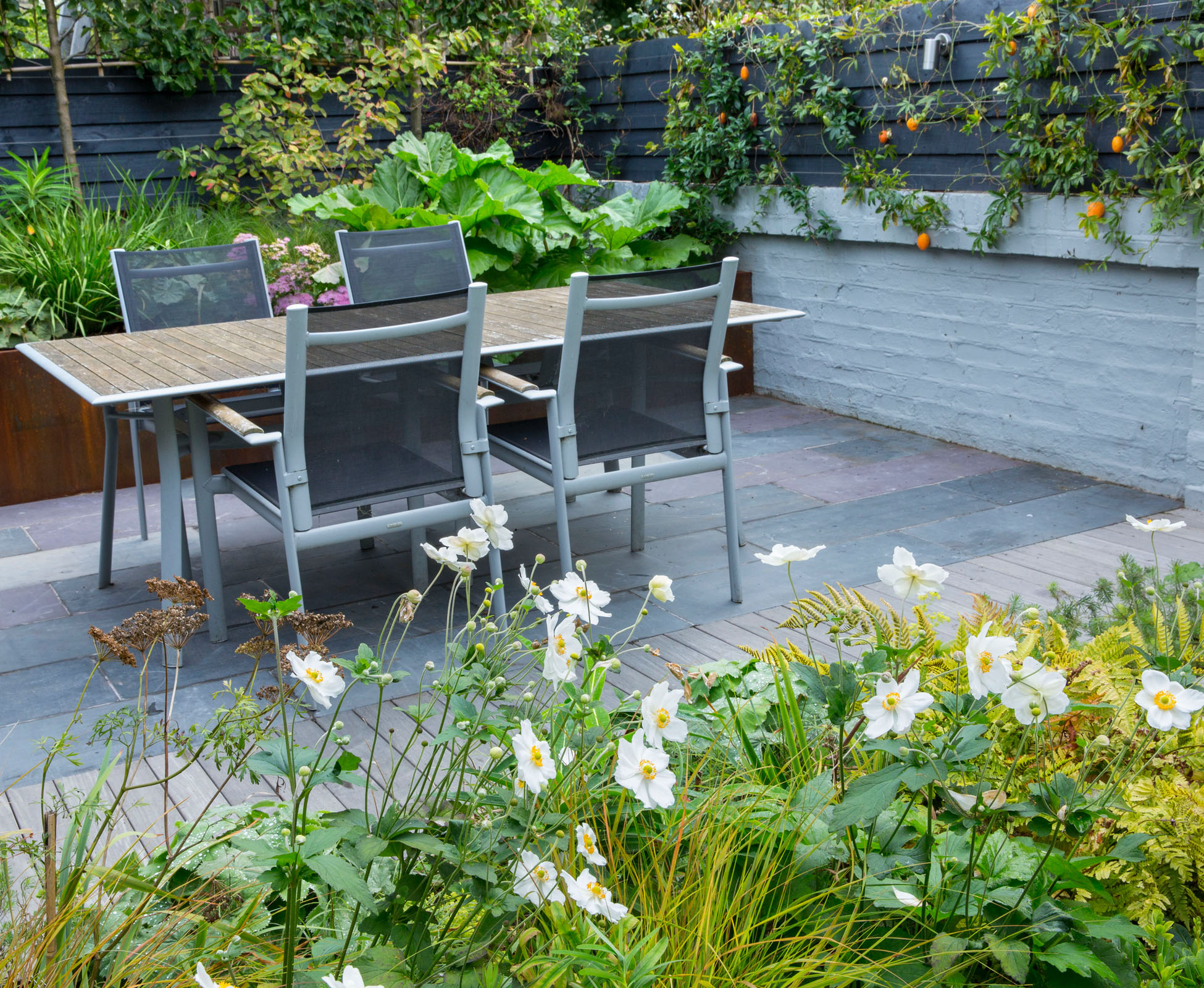 The rear of the garden can accommodate a table and chairs to enjoy the evening sun in this North London garden. The slate paving is delineated with a hardwood ipe deck strip, in line with a detail in the existing brick wall. At the back, a Corten steel retaining wall becomes a raised planter, full of herbaceous and some pleached trees.