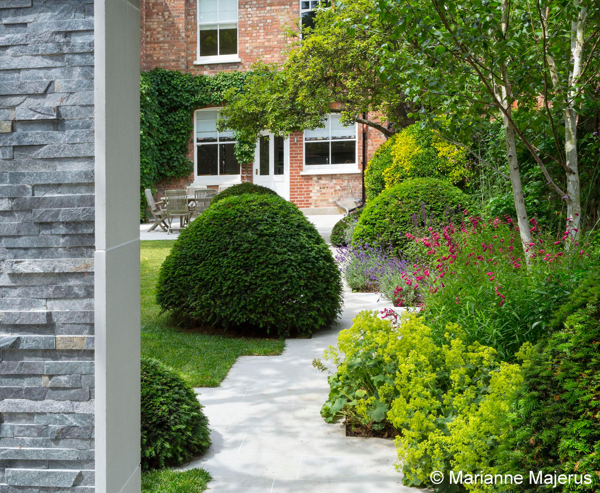 The slate wall feature acts like a door to the garden, hiding the parking space behind and inviting one to take the path leading home. It is a clear separation between two spaces, yet it blends in the whole garden nicely and becomes a focal point from the house. 