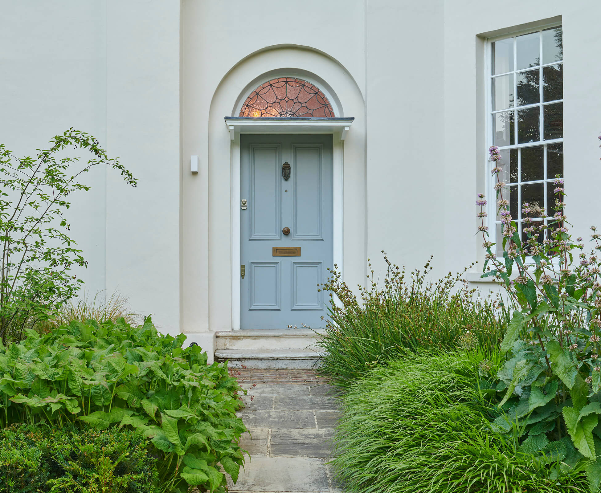 At the front of the house, soft grasses and Persicaria lean gently over the path, softening edges and creating a welcoming frame around the entrance.