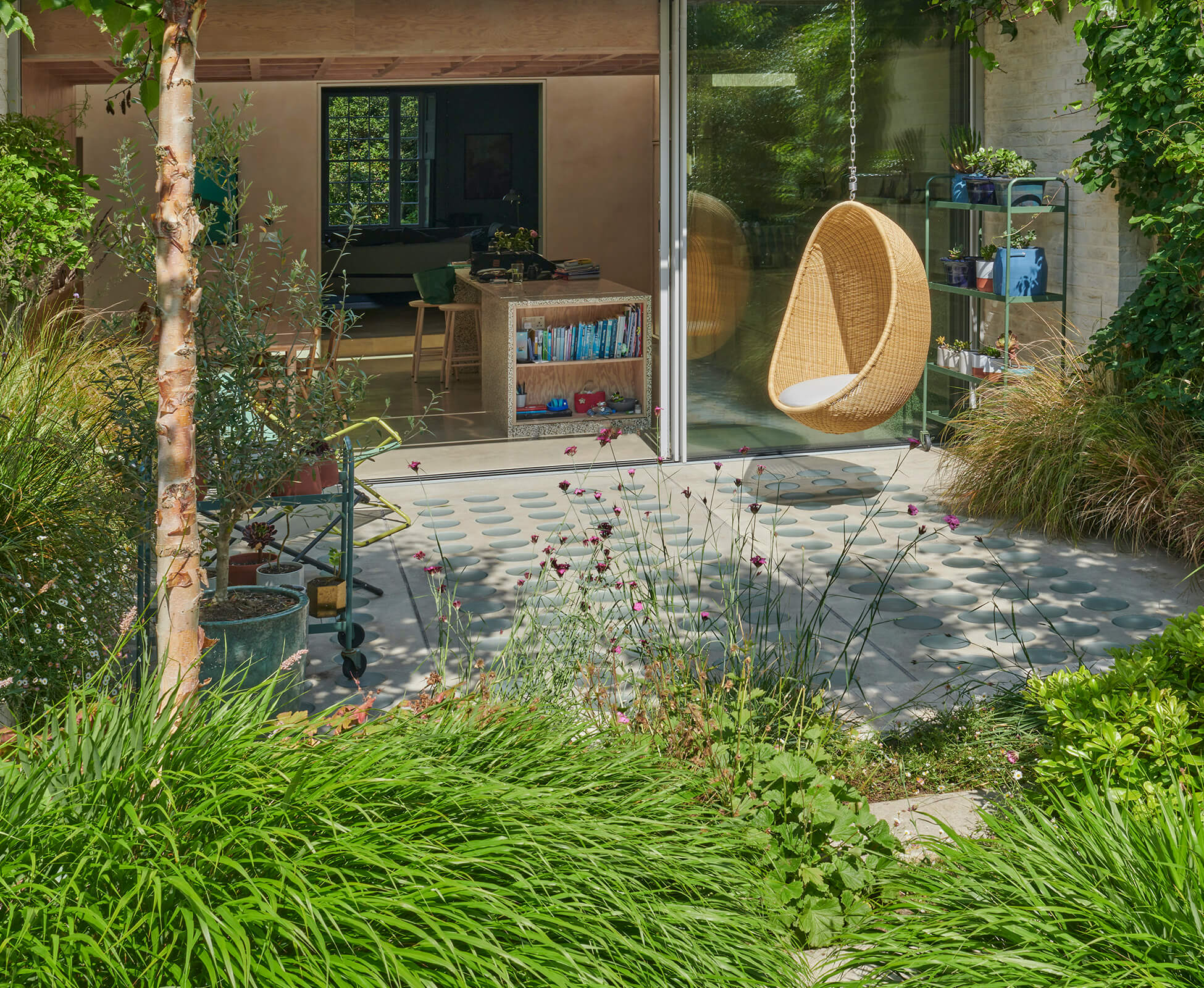 View of the main patio, designed by Proctor & Shaw Architects, with Hakonechloa and Anemanthele grasses spilling over the edges and framing the space, the iconic Nanna Ditzel pod chair hangs from the brise soleil.