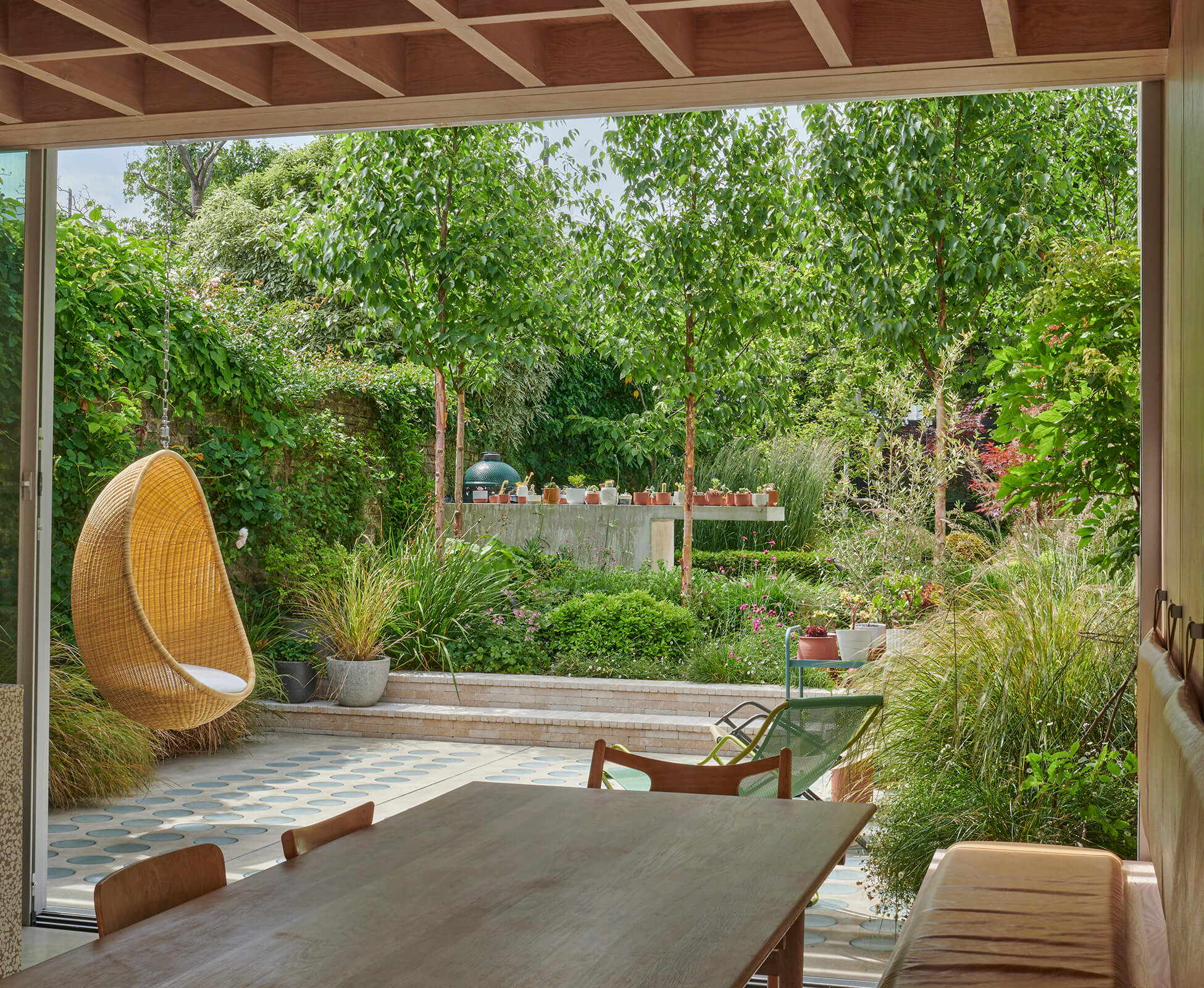Stunning view from the newly refurbished extension, designed by Proctor & Shaw Architects, showing the rear garden with organic planting that softens the edges and surrounds the main patio with greenery.