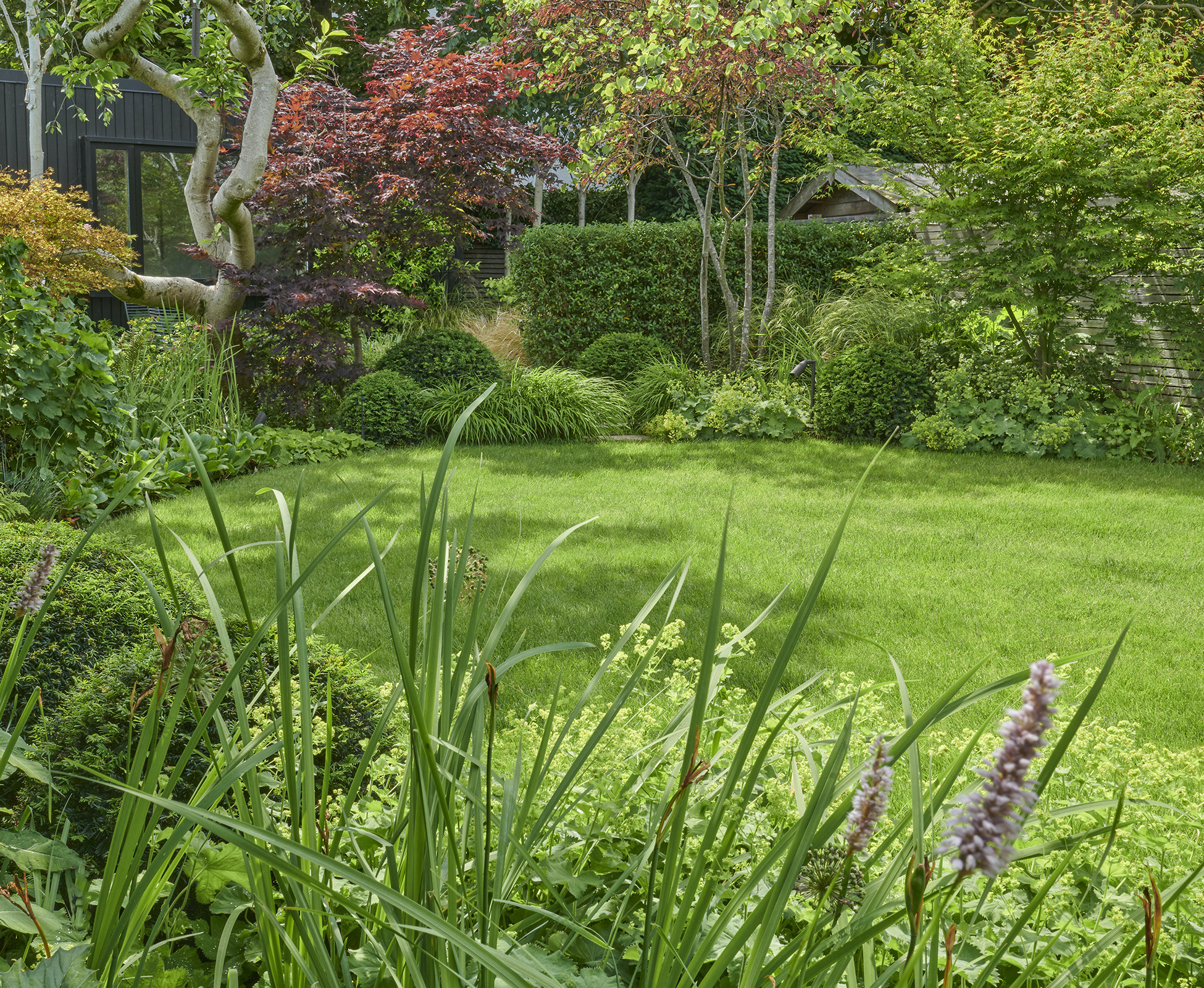 The garden lawn is oval-shaped, providing space for the clients to relax under the dappled shade of the surrounding trees.