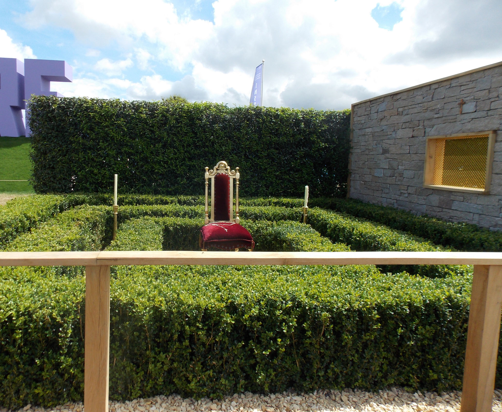 This conceptual garden designed on the theme of the seven deadly sins, expresses Greed at Hampton Court Palace Show Garden. View of one half of the space, showing the clipped hedges, and geometrical layout, in front of a tall evergreen background.