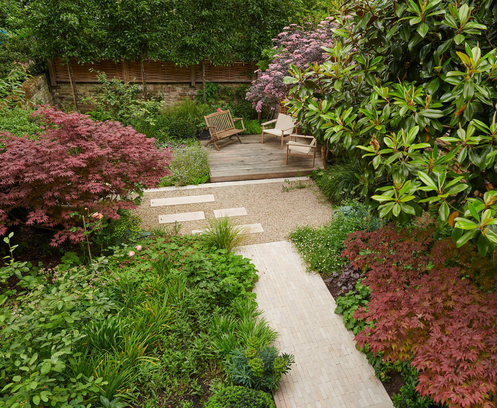 In this naturalistic Highbury garden a limestone paver focal path leads through soft planting to a raised oak seating spot under a cantilevered pergola enveloped in Wisteria.