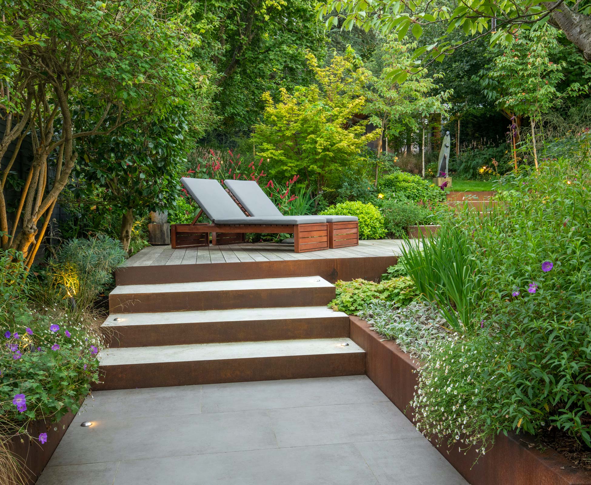 Corten steel risers and planters offer a striking contrast with the light toned sandstone treads while the surrounding plants spill over the edges softening the straight lines.