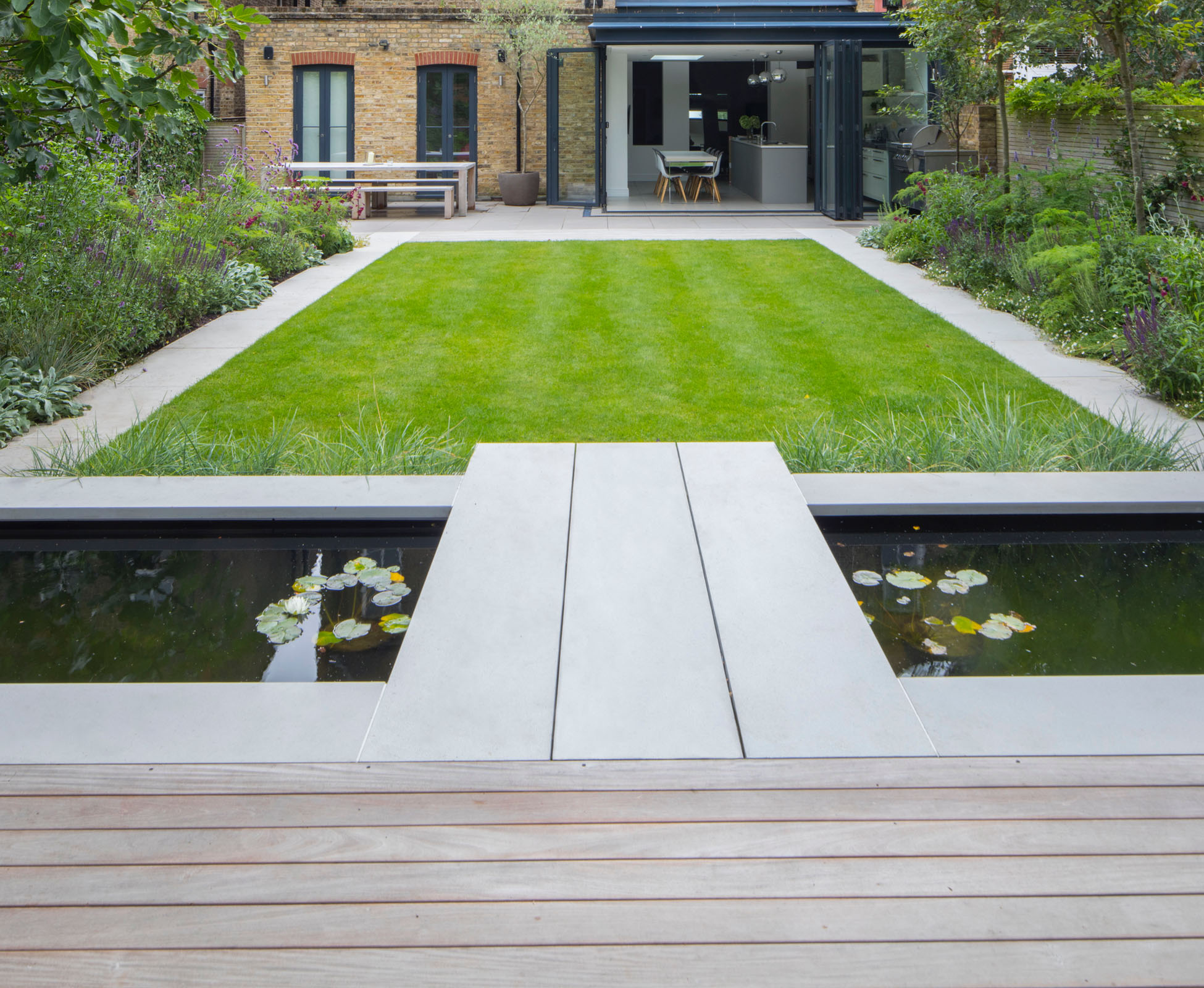 The lawn of this Islington garden is bordered by two sandstone paving strips and then some herbaceous planting to soften the boundaries. Waterlilies in the basin bring some life to the stillness.