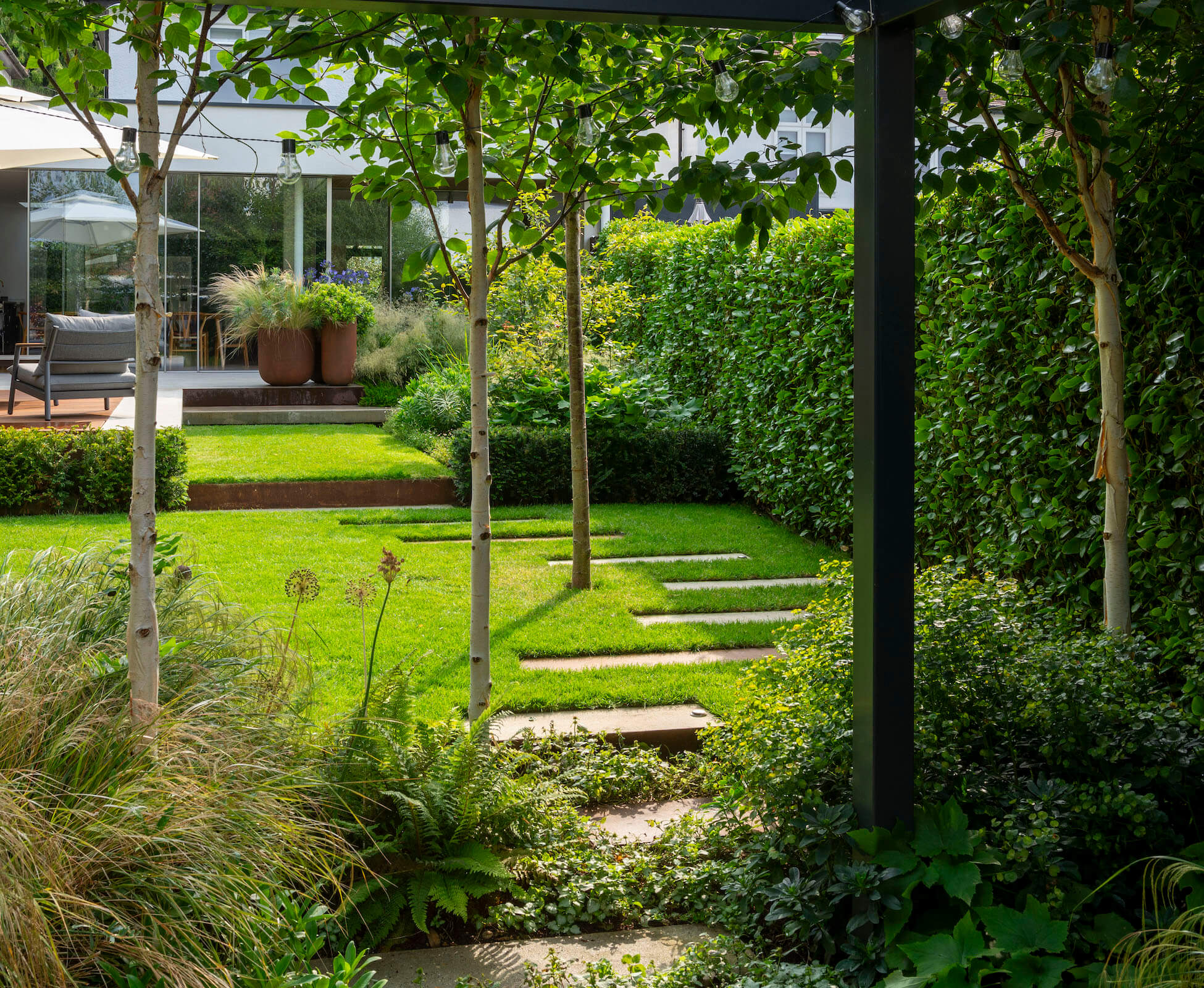 A pergola creates an intimate seating area with hanging pod chairs. framing the view back to the house.