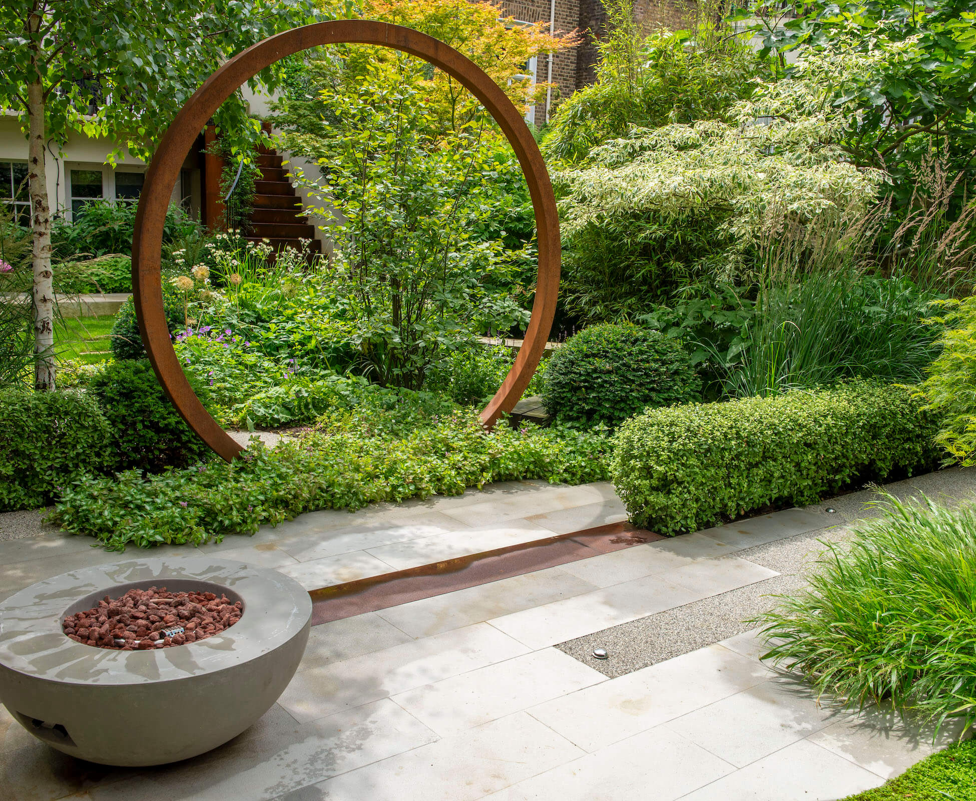 The circular Corten arch separates the herbaceous planting and lawn area from the rear seating and dining spot. Foliage colours and textures play an important role in the design of this garden.