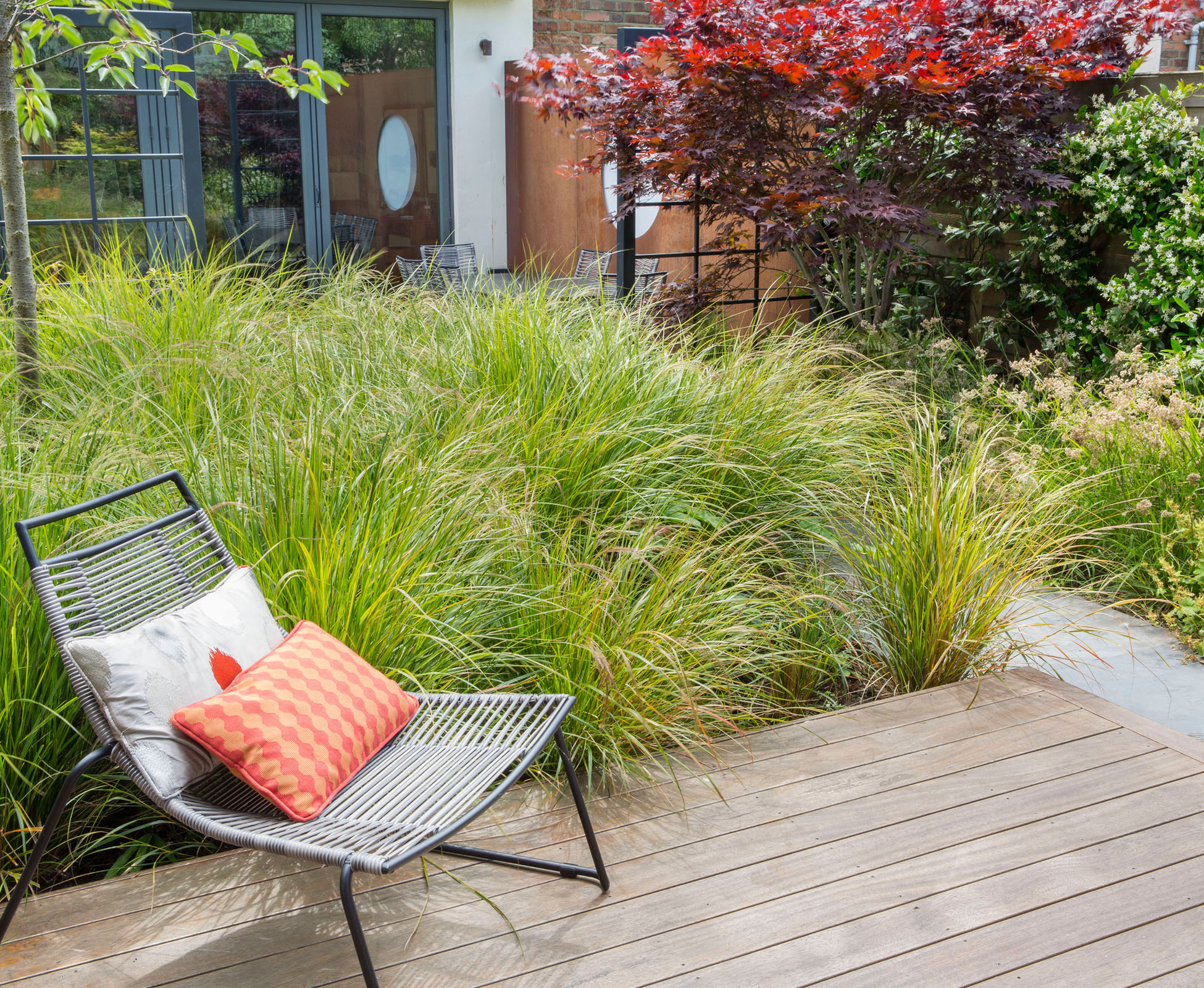 A cosy chair to rest on the hardwood ipe deck, near a corten feature fire pit, recessed into the deck. The planting act as a separation between spaces, here with evergreen grasses against a powder coated steel frame.