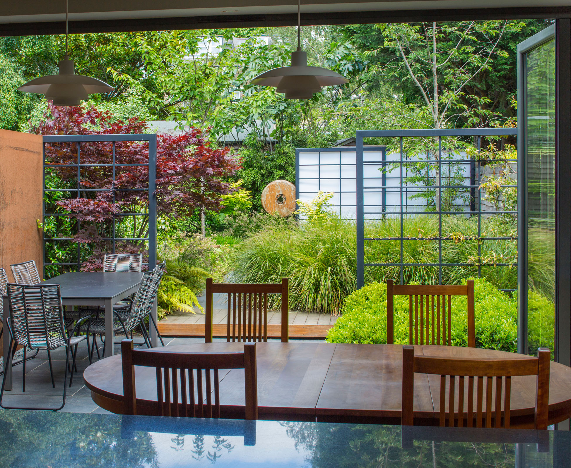 A wide view of this Queen’s Park garden from the kitchen, showing the effect of the steel frames dividing the garden; organising the space whilst making it look deeper. The eye bounces on the alternate features such as the japanese maple or the corten panel and sculptures. 