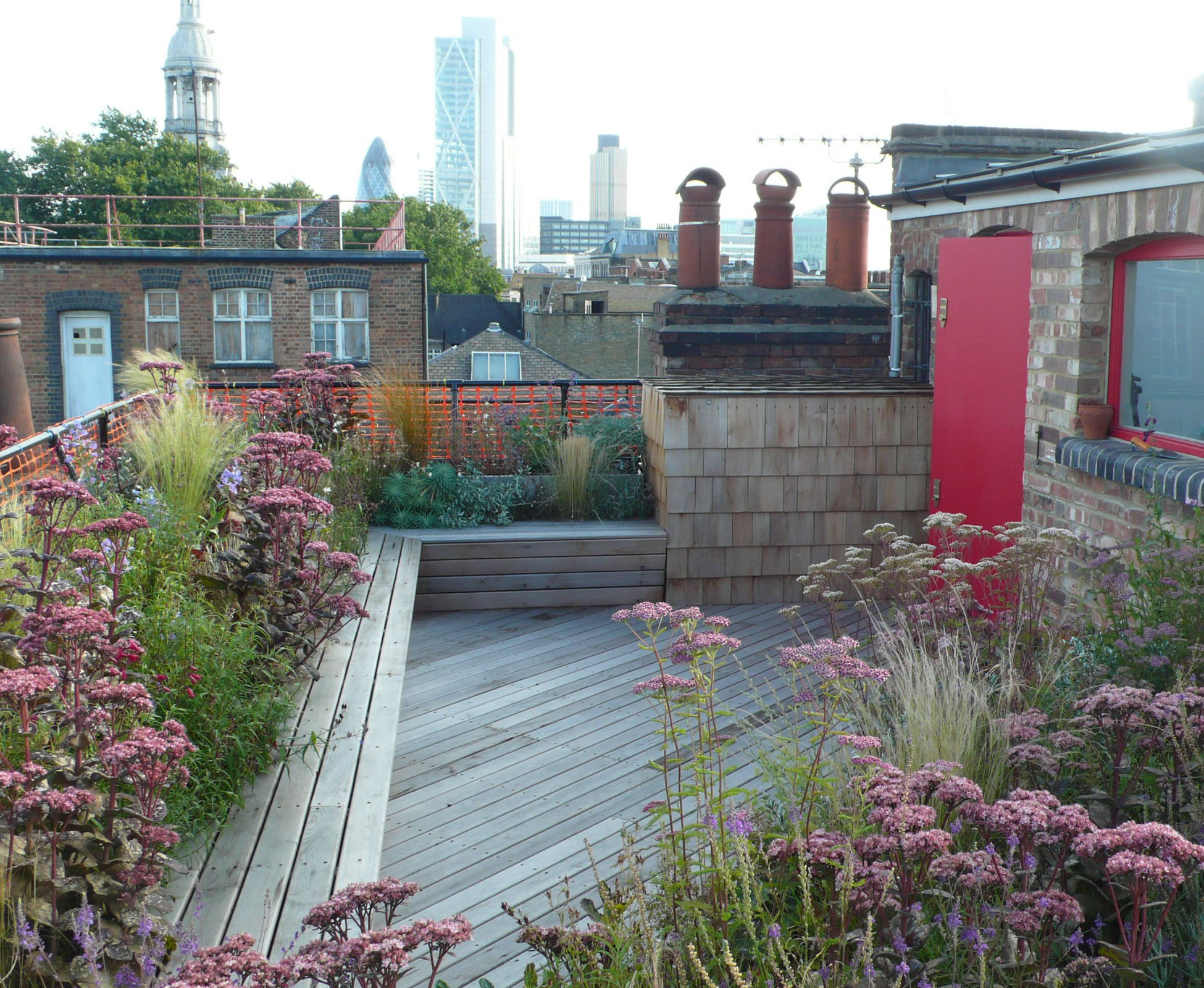 The decking boards have been laid with an angle to contrast with the built in cedar bench, wrapping around this rooftop in Shoreditch. The seat becomes a security barrier and delinitates the planting beds.