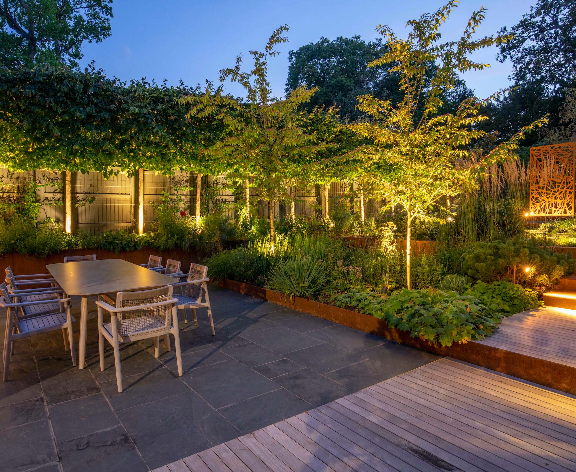 Soft herbaceous planting surrounds the lower dining area beautifully lit up at dusk.