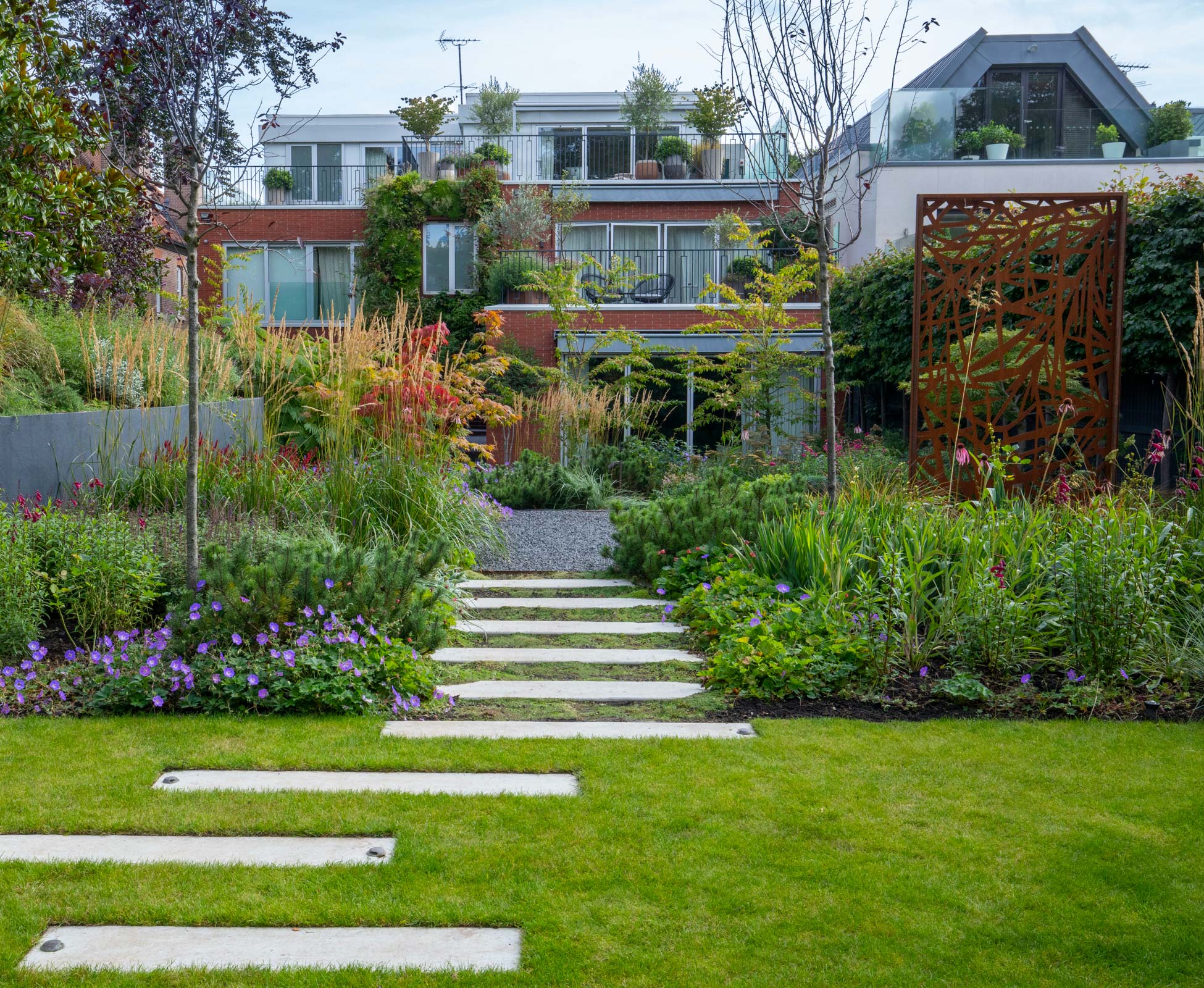 A staggered path through the lawn and planting leads back from the hidden ‘Den’ to the house patio, offset with dwarf mountain pine shrubs.