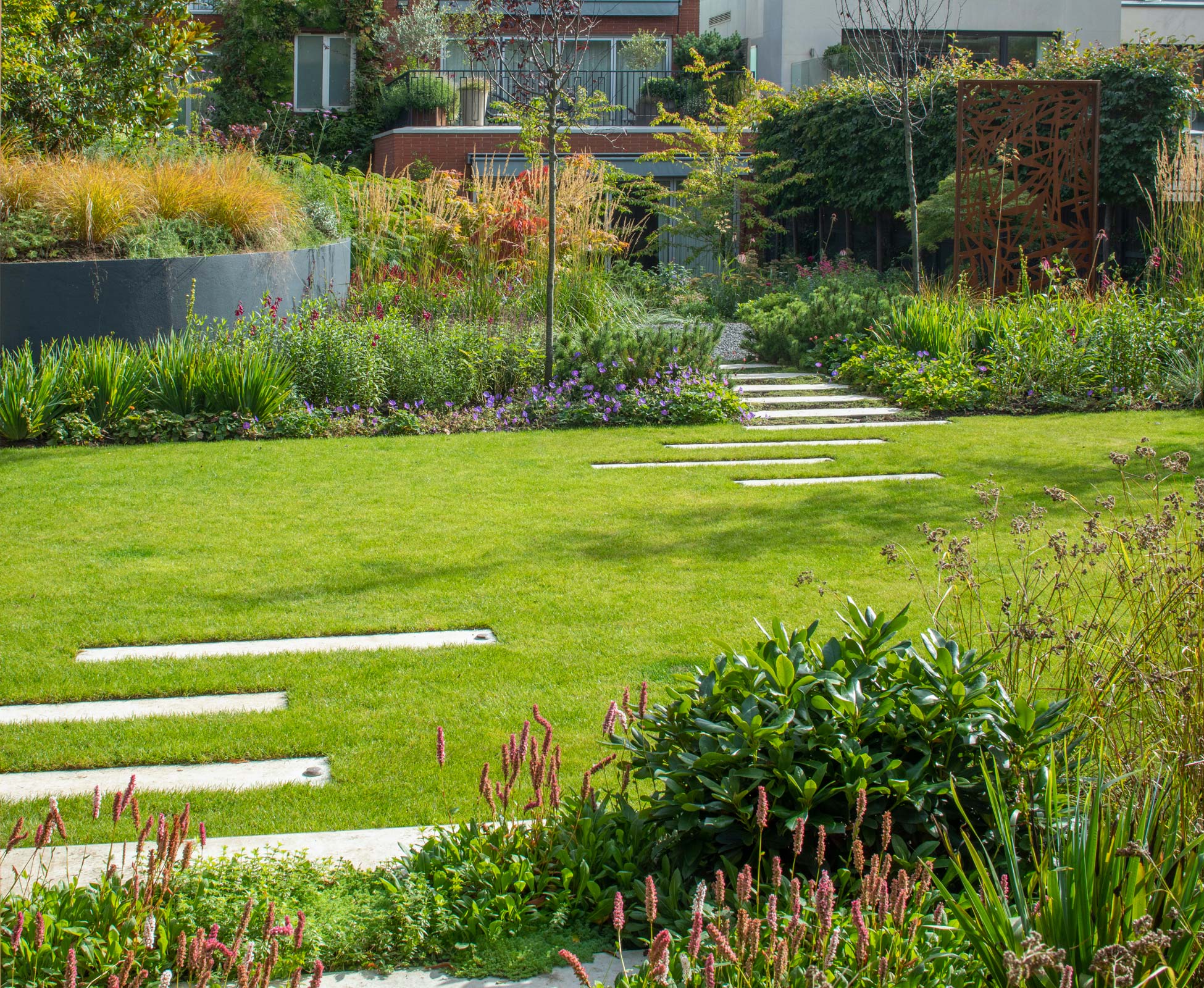A staggered path through the lawn and planting leads back from the hidden ‘Den’ to the house patio, offset with dwarf mountain pine shrubs.