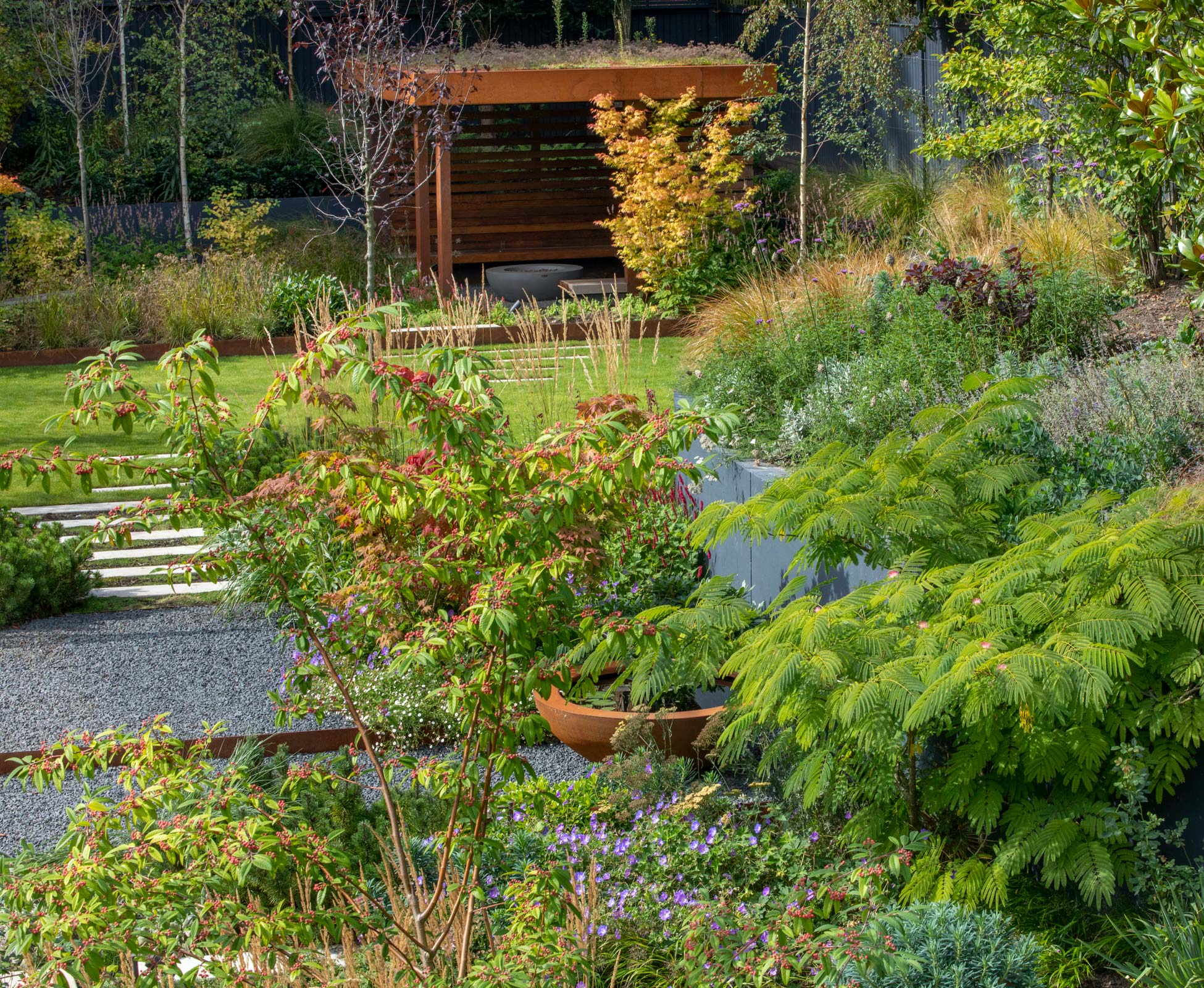 A staggered path through the lawn and planting leads to the hidden ‘Den’; it’s the perfect cozy corner to seat and enjoy the view of the garden while warming up in front of the fire pit.