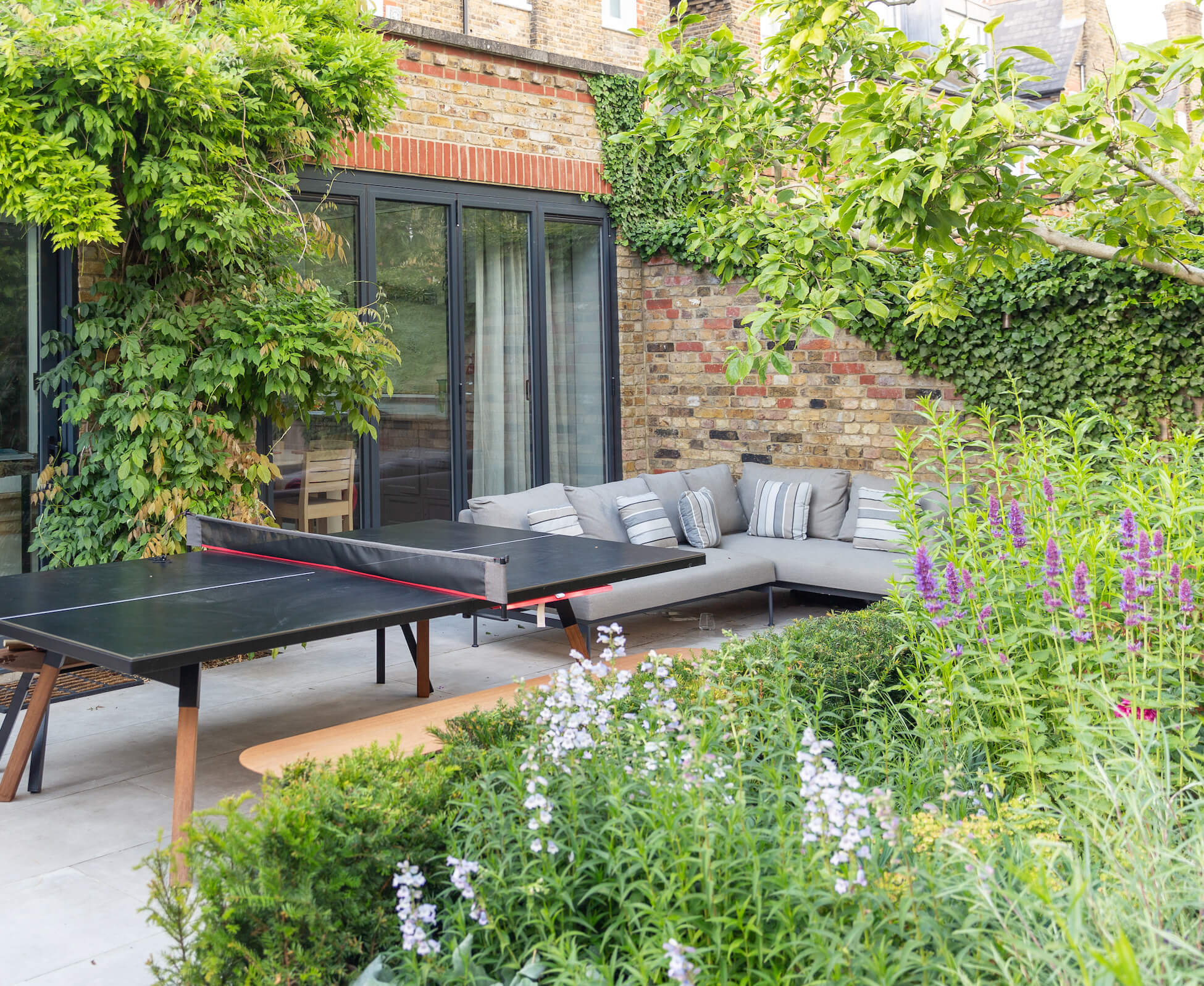 The patio was designed to be just big enough to accommodate a ping pong table, The deep herbaceous planting borders ensure that the seating area is enveloped in greenery.